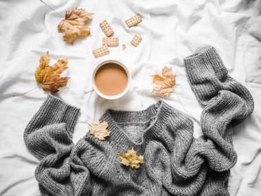 一杯咖啡, 灰暖针织毛衣超大, 黄色干叶子在床上-舒适的家庭静物, 顶部视图。复制空间