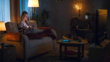 在晚上可爱的小女孩正坐在客厅沙发上，她看电视。她认为她柔软的玩具，房间灯光亮起