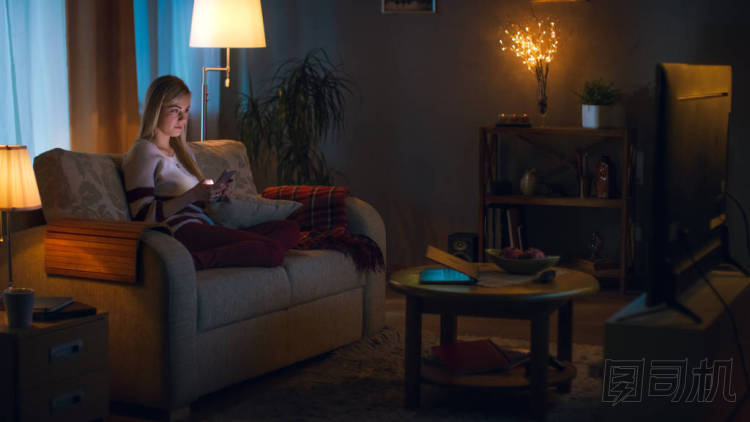 在晚上可愛的小女孩正坐在客廳沙發(fā)上，她看電視。她認為她柔軟的玩具，房間燈光亮起