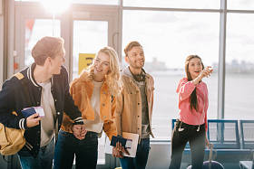 在机场持有护照、登机牌和行李的微笑的年轻朋友