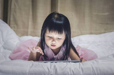 小女孩躺在床上晚上使用互联网观看电视或 gamp 玩儿童智能手机或片剂上瘾概念