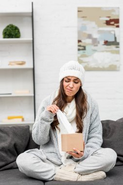 在溫暖的衣服生病的年輕婦女坐在沙發(fā)上從盒子里拿餐巾紙