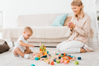 可愛的幼兒玩五顏六色的立方體和母親在托兒所室