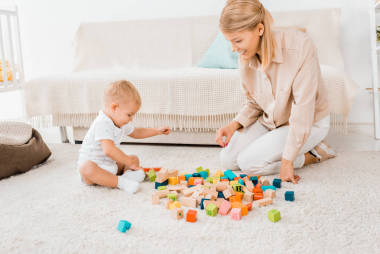 可愛的幼兒玩五顏六色的立方體和母親在托兒所室