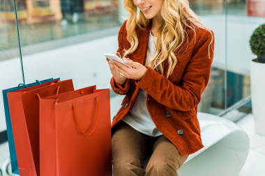 裁剪的婦女使用智能手機(jī)和坐在購物袋的看法