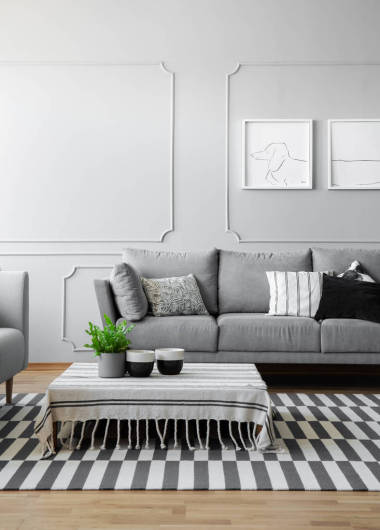 在現(xiàn)代客廳里, 用灰色色調設計的用條紋桌布覆蓋著低咖啡桌上的咖啡杯和盆里的綠色植物