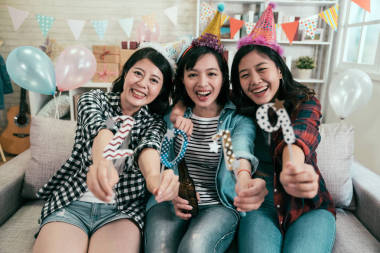 有魅力的女孩慶祝新年前夜的房子聚會。年輕的朋友顯示2019年數(shù)字的相機微笑愉快地坐在沙發(fā)上。美麗的亞洲婦女室內(nèi)生活方式概念