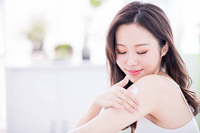 年轻的护肤妇女在家里的胳膊和肩膀上涂身体化妆水
