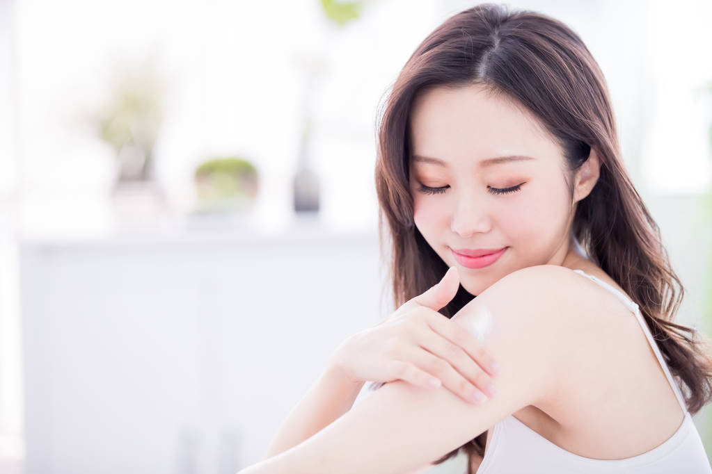 年轻的护肤妇女在家里的胳膊和肩膀上涂身体化妆水