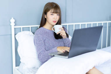 在床上工作的亞洲女人。她穿毛衣紫羅蘭色。上午檢查電子郵件互聯(lián)網(wǎng)從筆記本