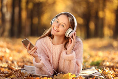 年輕美麗的女孩躺在耳機和智能手機在秋天公園