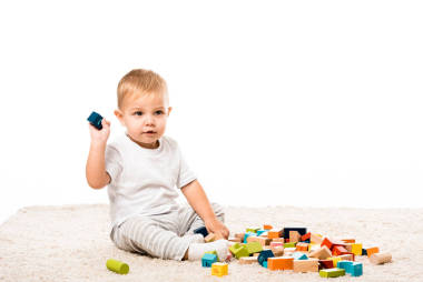 可愛的幼兒男孩坐在地毯上, 玩彩色木塊隔離在白色