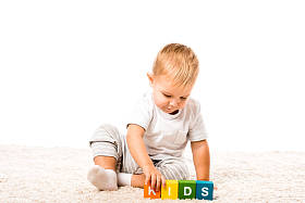 可爱的幼儿男孩玩彩色立方体与文字地毯上孤立的白色