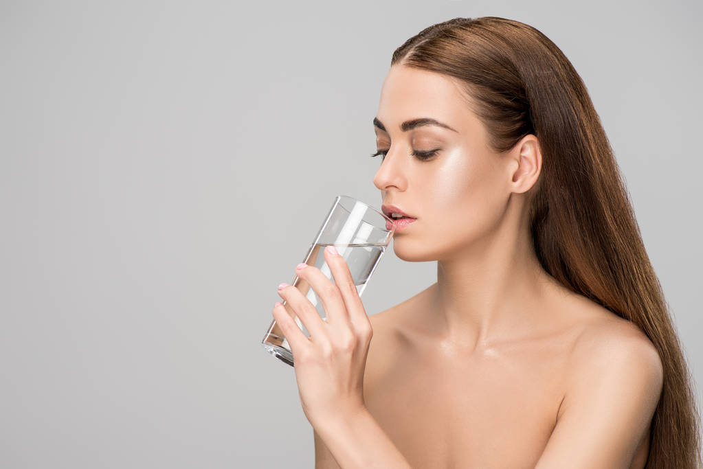 美丽的裸体妇女喝纯净的水隔离在灰色