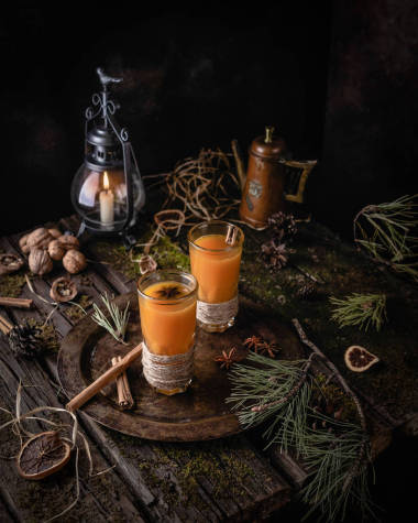 熱山沙棘飲料與香料在高眼鏡在復古托盤在松樹分枝之間與冬天裝飾在老木