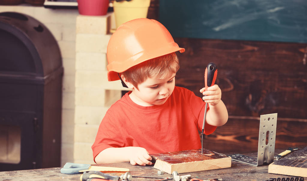 童年的概念。男孩在橙色硬帽子或头盔, 学习室背景。孩子梦想未来的建筑或建筑事业。男孩扮演建设者或修理工, 使用工具 童年的概念。男孩在橙色硬帽子或头盔, 学习室背景。孩子梦想未来的建筑或建筑事业。男孩扮演建设者或修理工, 使用工具