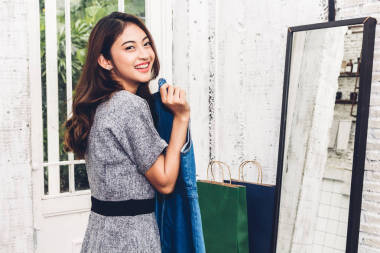 快乐的女人购物和选择的衣服, 看着镜子在一个商店与五颜六色的购物袋. 时尚购物理念