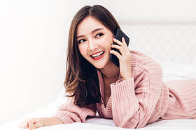 快乐的女人放松使用和交谈的智能手机在家里的床上. 技术与沟通理念