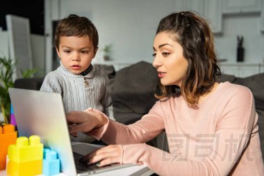 有吸引力的女人指著筆記本電腦屏幕, 她的小兒子在家