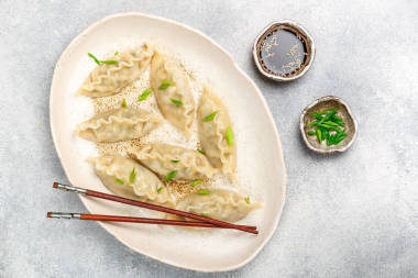 韩国饺子, 肉和蔬菜放在白色的盘子里, 芝麻、酱油和青葱放在灰色的混凝土表面。亚洲美食。选择性对焦