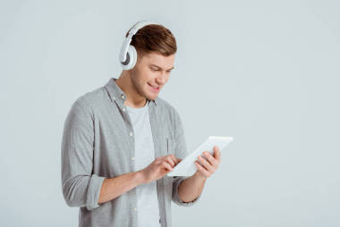 英俊的男人在耳機(jī)聽音樂, 并使用數(shù)字平板電腦孤立在灰色