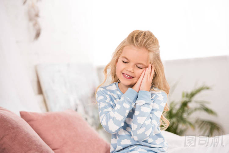 可愛的昏昏欲睡的孩子坐在床上閉著眼睛 