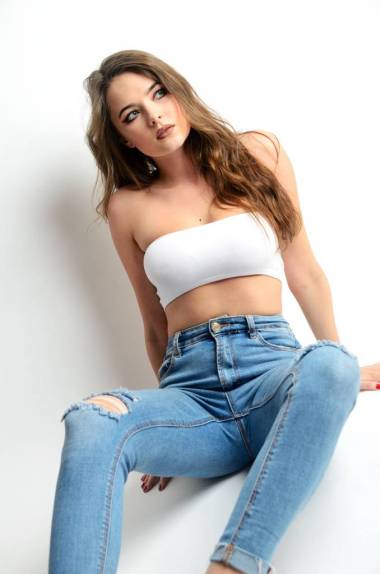 有吸引力的年輕女子的肖像與牛仔褲和白色上衣。坐在地上的身材造就的女性模特