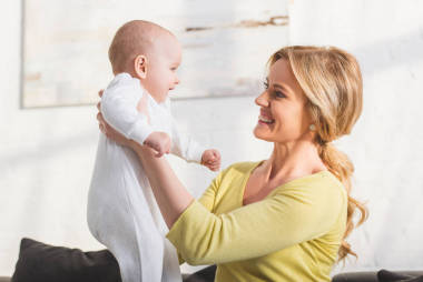 幸福的母亲抱着可爱的婴儿在家的侧视图 