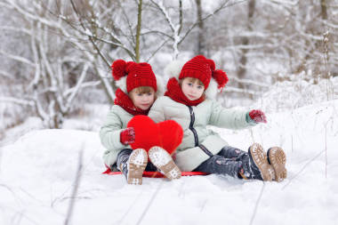有趣的姐妹雙胞胎坐在雪地上, 在冬季公園散步時(shí), 手里拿著一顆巨大的紅心