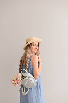 美丽的年轻女子与花束的花和背包在灰色背景