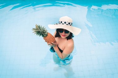美麗的女人在游泳池里放松的肖像, 同時(shí)拿著菠蘿, 戶外和暑假的娛樂運(yùn)動(dòng)