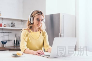 有吸引力的金發(fā)碧眼的女人聽(tīng)音樂(lè)在耳機(jī), 而使用筆記本電腦