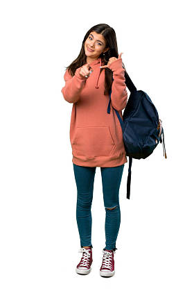 一个少年女孩的全长镜头与运动衫和背包做电话手势和指着前面