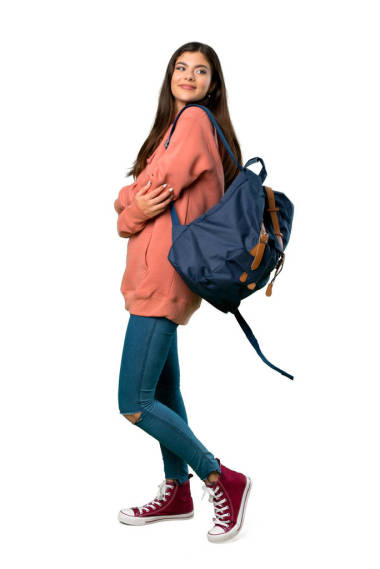 一個穿著運動衫和背包的少年女孩面帶微笑地看著肩膀的全長照片