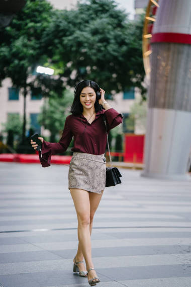 美麗的韓國女人穿著一件優(yōu)雅的襯衫和短褲跳舞, 她走在城市的街道上, 戴著耳機