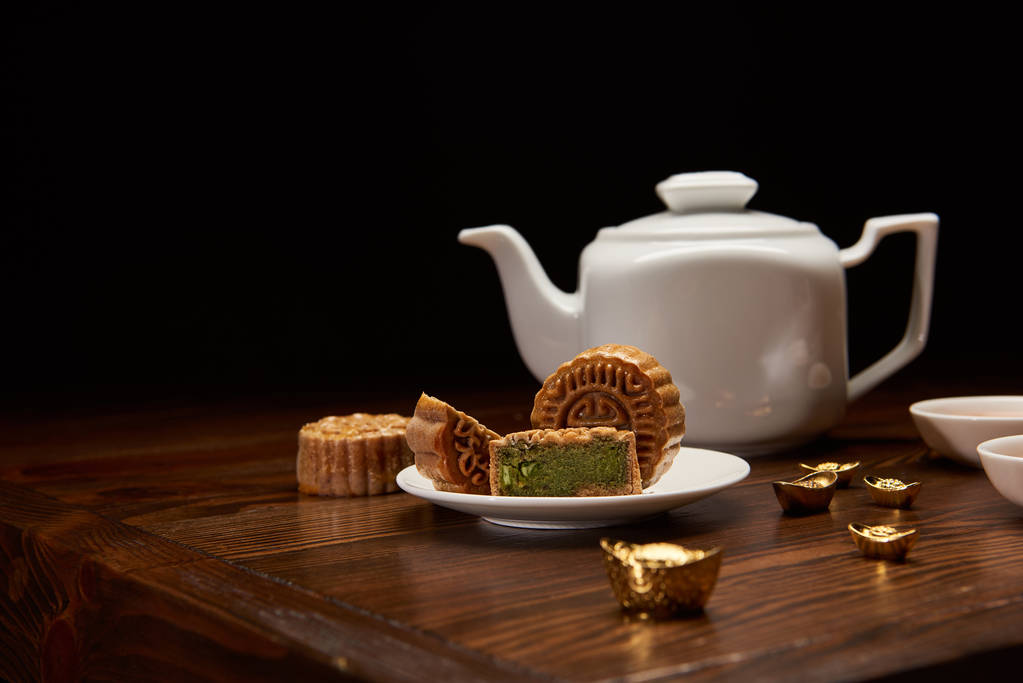 传统美味的中国月饼, 茶壶和金锭在木桌上隔离在黑色
