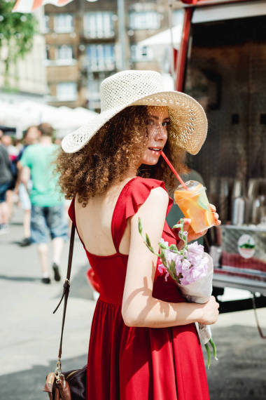 年輕的卷曲的女人在草帽與冷果汁杯子拿著溫柔的花束 