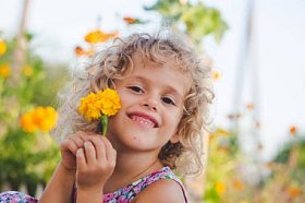 微笑的卷曲的女孩的画像摆与黄色万寿菊花