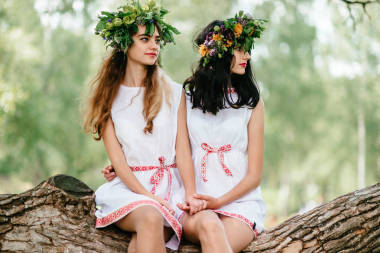 年輕的美麗的婦女在民族服裝休息在倒下的樹