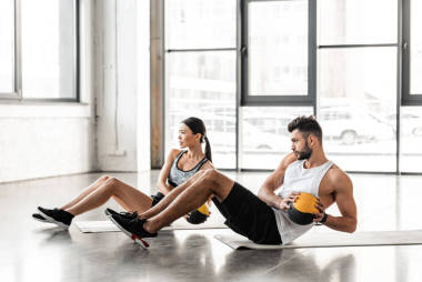 运动年轻夫妇在运动服装手持药丸和在健身房的瑜伽垫锻炼的侧视图