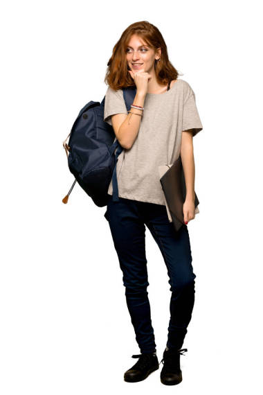 一個(gè)年輕的紅頭發(fā)的學(xué)生在孤立的白色背景上, 用手放在下巴上, 向一旁看的全長(zhǎng)照片