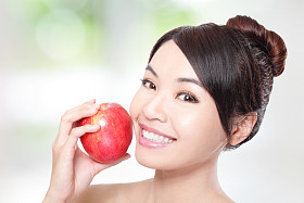 年轻女子吃红苹果与健康牙齿照片