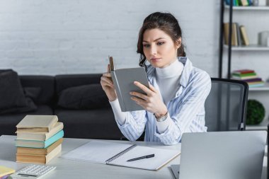 心煩意亂的婦女學習與書籍附近的筆記本電腦在現代辦公室