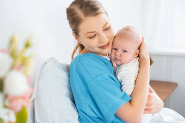 快樂的年輕母親坐在病床上擁抱可愛的嬰兒 