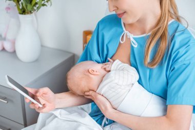 微笑的母親母乳喂養(yǎng)嬰兒和使用智能手機(jī)在病房的照片