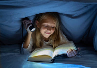 快樂聰明的女孩讀童話般的書躺在黑暗中的被套床下拿著一盞燈籠在閱讀技能文學(xué)學(xué)校的成功和教育的概念