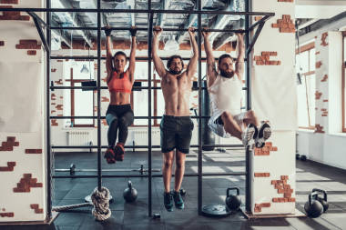 運(yùn)動員們用一根溺水的腿掛在水平酒吧上。培訓(xùn)日。健身俱樂部。健康的生活方式。有實(shí)力的人?；顒蛹倨?。交叉的概念。明亮的健身房。新聞練習(xí)