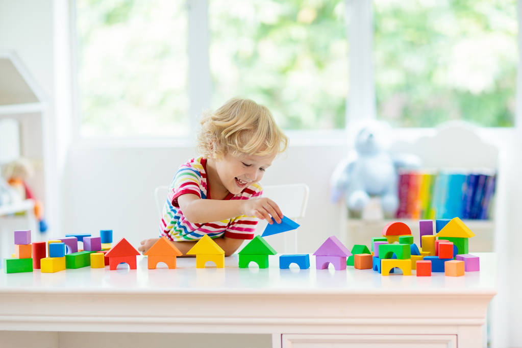 孩子玩五颜六色的玩具块。小男孩建筑塔的块玩具。为幼儿提供教育和创意玩具和游戏。婴儿在白色的卧室与彩虹砖。儿童在家