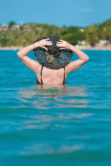 黑发妇女在黑帽子和太阳镜在蓝色海摆姿势拍照