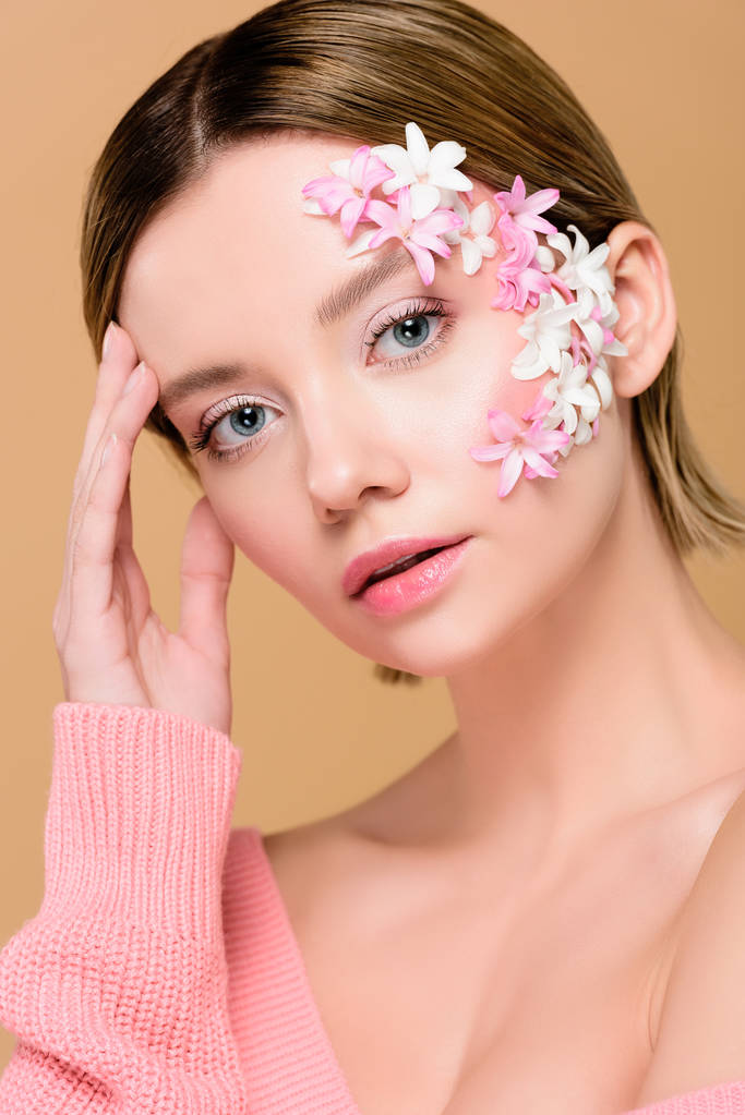 美丽的女人与鲜花在脸上看着相机孤立的米色